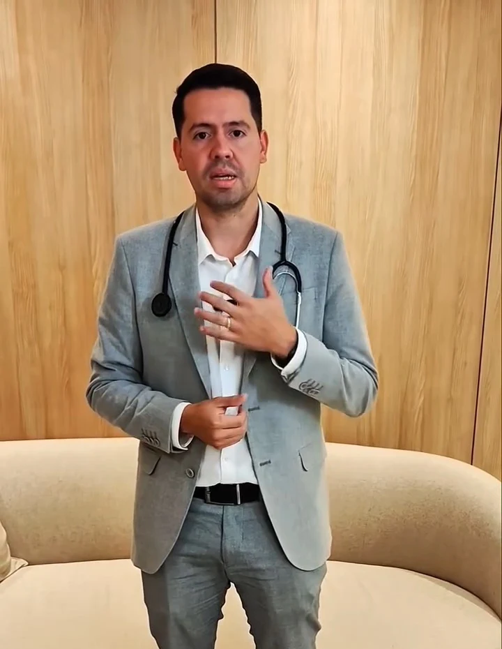 Dr. Caio Blanch, de blazer cinza e estetoscópio, diante do sofá curvo creme do Instituto